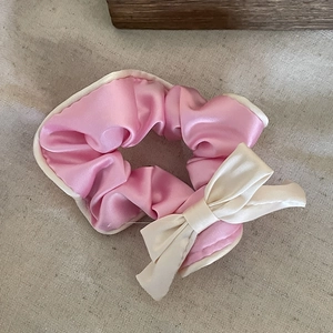 Pink satin bow scrunchie with white piping on a textured beige background