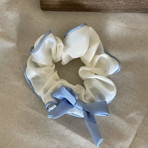 Elegant white silk scrunchie with light blue trim and ribbon bow on linen background