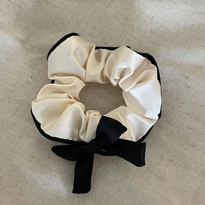 Detail of cream satin scrunchie with black trim and elegant bow on textured background
