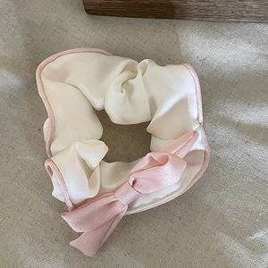 Detailed macro of silk satin scrunchie with pink bow and elegant two-tone trim finish