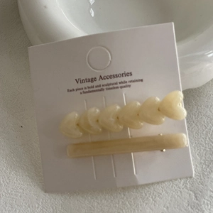 Two-piece cream heart hair clip set with vintage accessory card on neutral background