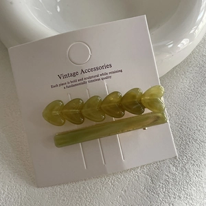 Two-piece avocado green heart hair clip set with resin finish on display card