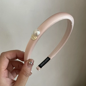 Detail of pink satin padded headband featuring a large pearl and gold logo charm