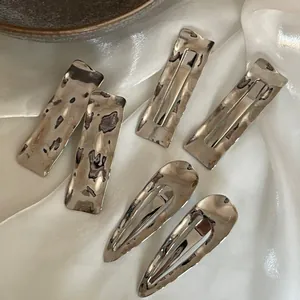 Detail of silver wave hair clips with hammered metal texture on white silk fabric background