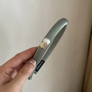 Detail view of sage green satin headband with large faux pearl and gold metal emblem