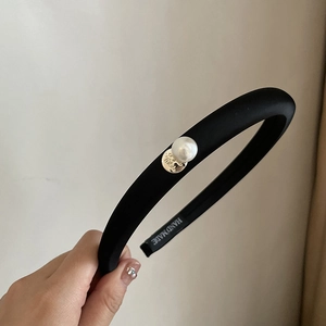 Close-up of black padded sponge headband featuring a white pearl and handmade gold stamp