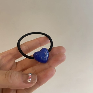 Detail of blue acrylic heart pendant with golden text on black elastic hair tie