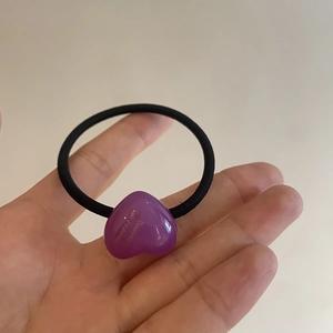 Detail of purple acrylic heart charm with gold lettering on a black elastic hair tie