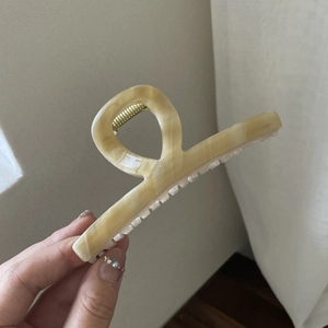 Detail of cream marble acetate hair claw clip with golden spring held in hand