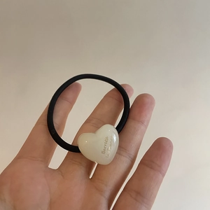 Detail of black elastic hair tie featuring white acrylic heart charm with printed text