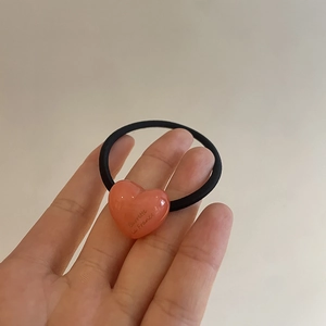 Close-up of a pink heart resin pendant on a black elastic hair tie with engraved text