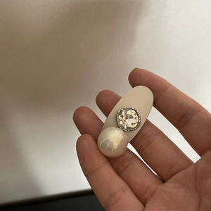 Vista dettagliata di un fermaglio ovale con perla bianca e strass con bordo in argento