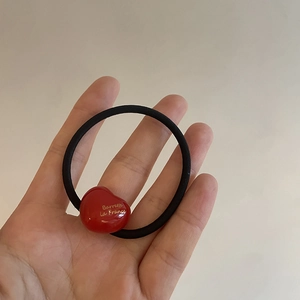 Detail of red acrylic heart pendant on black elastic hair tie with golden lettering