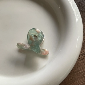 Mini marble-patterned acetate hair claw in green and pink, resting on a ceramic dish