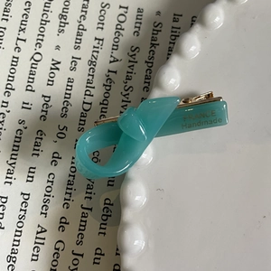 Detailed close-up of a teal handmade bow hair clip on a white plate with French text