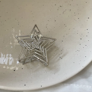 Silver star-shaped metal hair claw clip with rhinestones in a white ceramic bowl