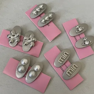 Brushed silver hair clips set with rhinestones, pearls, and saturn motifs on pink card