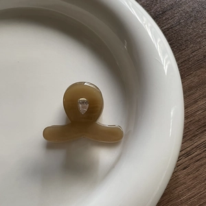 Top view of a mini amber resin hair claw clip with a silver spring on a ceramic plate