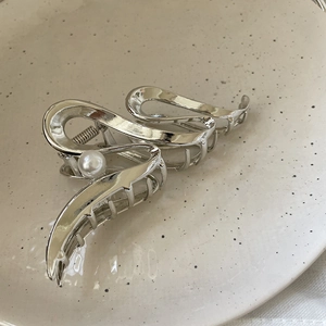 Detail shot of a silver metal hair claw clip with a white pearl on a ceramic plate