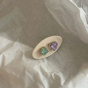 Close-up of heart and square crystal stud earrings on a beige display card