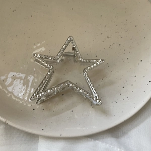Macro view of star-shaped silver metal hair claw clip with textured surface on ceramic tray