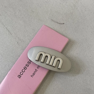 Close-up of brushed silver metal hair clip with rhinestone letter detail on pink card