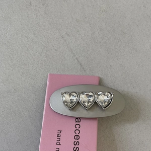 Close-up of silver oval hair clip featuring three sparkling heart-shaped rhinestones
