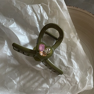 Elegante pinza per capelli verde oliva con strass colorati su sfondo di carta stropicciata