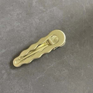 Goldene gewellte Haarspange aus Metall mit minimalistischem Design auf dunklem Stein
