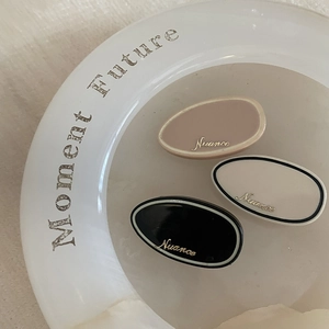 Close-up of three acetate hair clips with gold logo on a white minimalist plate