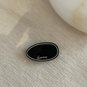Minimalist black acetate duckbill hair clip with golden Nuance lettering and retro style