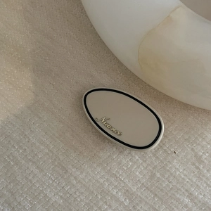 Elegant cream acetate hair clip with black border and gold Nuance logo on white linen
