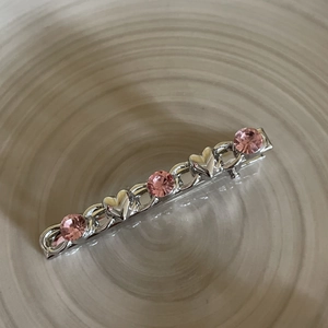 Elegant silver metal hair clip with pink gemstones and heart accents on a beige plate