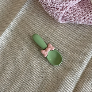 Cuillère à dessert verte mignonne avec nœud rose sur fond de tissu beige minimaliste
