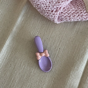 Détail d'une pince à cheveux nœud mauve sur tissu beige avec accents décoratifs roses