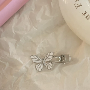 Elegant silver butterfly hair clip with white enamel wings on minimalist paper background