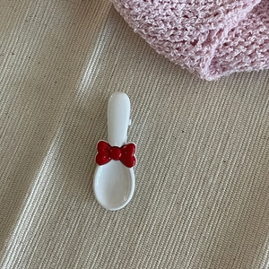 Pince à cheveux créative en forme de cuillère blanche avec un nœud rouge sur tissu doux