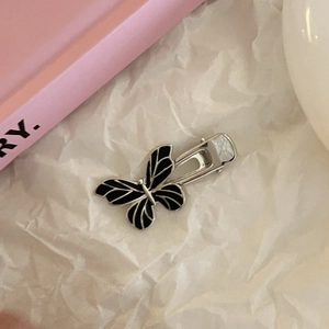 Silver butterfly hair clip with black enamel detail on minimalist white paper texture