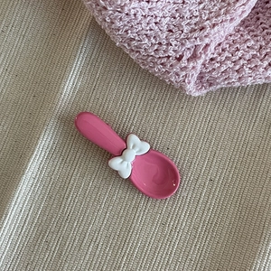 Gros plan d'une cuillère rose vif avec un nœud blanc sur un tissu texturé crème doux