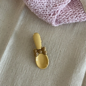 Détail d'une pince à cheveux jaune en forme de cuillère avec nœud sur tissu rayé
