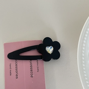 Detail einer schwarzen Blumen-Haarspange mit buntem Kristallherz auf rosa Karte