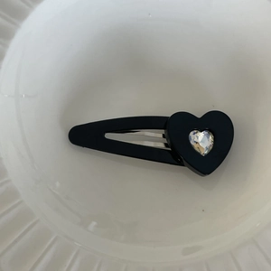 Schwarze Herz-Haarklammer mit glitzerndem Strassstein auf einem weißen Keramiktablett