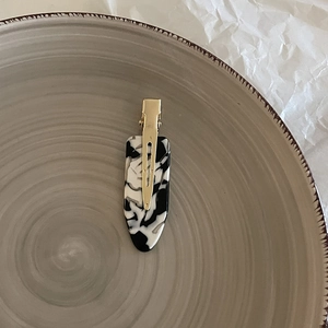 Detailed macro view of marbled acetate duckbill hair clip on a minimalist ceramic dish