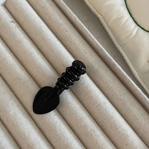 Glossy black heart shovel hair clip shown in a beige velvet jewelry display box