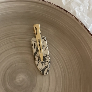 Close-up of marble pattern acetate hair clip with gold metal base on ceramic plate