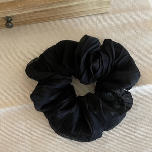 Dettaglio dell'elastico per capelli in tessuto nero plissettato su fondo crema