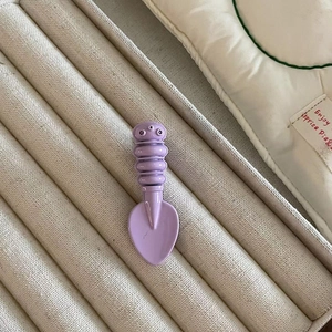Close-up of a purple candy-colored spoon hair clip on a beige striped fabric display case