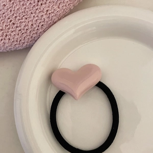 Vue détaillée d'un élastique à cheveux noir avec un cœur en résine rose sur un plateau