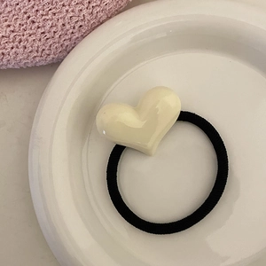Détail d'un élastique à cheveux noir avec un pendentif en forme de cœur en résine crème