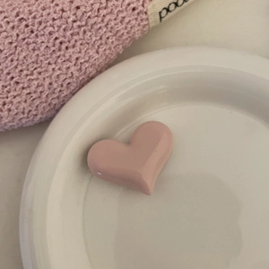 Vue détaillée d'une pince à cheveux cœur rose mat sur une assiette en céramique blanche